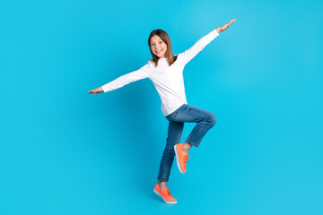 Fototapeta na wymiar Full length photo of good mood schoolgirl dressed white shirt jeans sneakers hold arms like wings isolated on blue color background