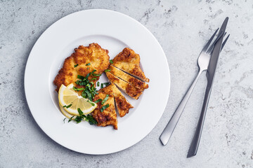 Schnitzel with slice of lemon on white plate on grey background