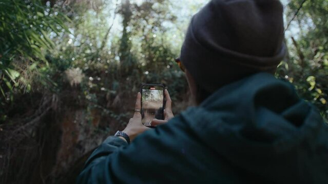 Female tourist taking photos of beautiful abandoned railway tunnel in national park with smartphone during hike. Rack focus, back view