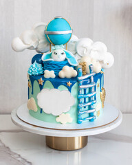 Beautiful blue birthday cake with fondant bunny, ladder, clouds and air balloon on grey background