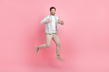 Full length photo of cool confident guy dressed teal shirt jumping high thumbs up isolated pink...