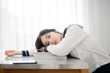 asian high school girl in japanese student uniform sitting sitting at desk for read a book with annoyed, bored, tired, bored emotion