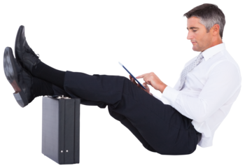 Businessman using digital tablet with feet up on briefcase