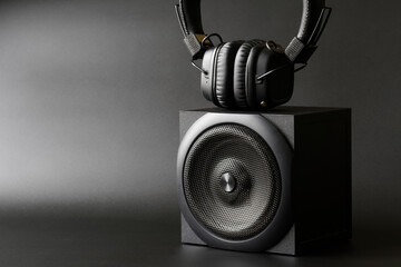 Black wireless headphones and an audio speaker on a dark background. Concept of technology in music...