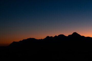 Black silhouette of mountains against the sky during sunset.