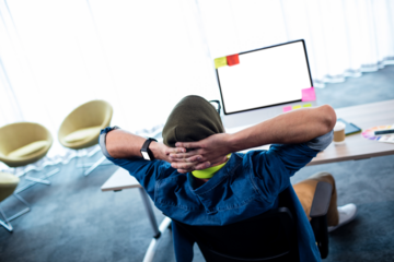 Man relaxing on chair with hands behind head by computer