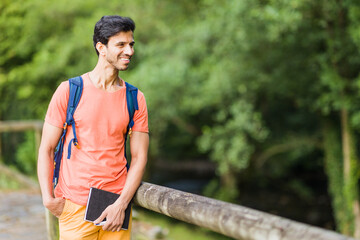 south asian 40s male hiking with a backpack in Asturias green countryside with a diary in spain.