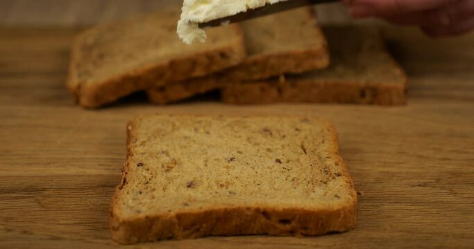 Cream cheese spread with a knife on a piece of multigrain bread on a wooden cutting board.