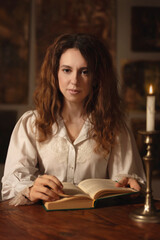 Beautiful woman in vintage clothes reading a book by candlelight in an art studio