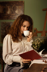Beautiful woman in vintage clothes reading a book by and drinking a coffee