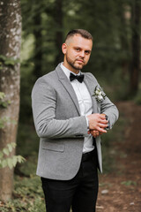 stylish groom adjusted his watch looking into camera lens. Luxury expensive watch on hand. Gray jacket, white shirt, ankle boots made of fresh flowers. Photo details