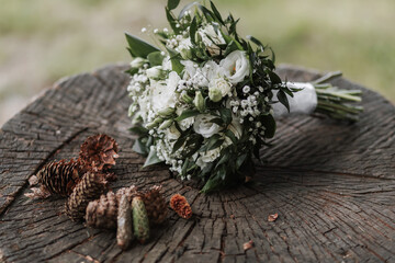 wedding bouquet of white flowers on a wooden stand on a spruce litter around many cones beautiful texture