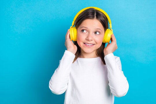 Photo of optimistic satisfied girl wear white long sleeve look empty space arms touching headphones isolated on blue color background