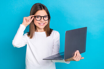 Photo of cheerful satisfied girl with long hairstyle wear white long sleeve touching glasses hold laptop isolated on blue color background