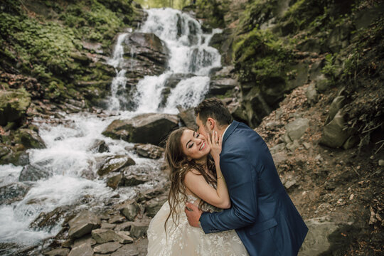 Portrait of a happy bride and groom near a waterfall. Bride and groom. Wedding photo session in nature. Photo session in the forest of the bride and groom.