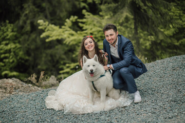 Bride with long hair, smiling sincerely, happy stylish groom, photo with dog. Wedding photo session in nature. Photo session in the forest of the bride and groom.