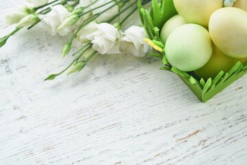 Happy Easter. Easter eggs and rabbit in green basket on white old wooden table with white and yellow roses. Spring Happy Easter holiday card.  Easter background with copy space. Top view.