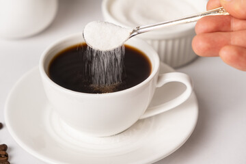 The process of pouring white sugar from a spoon into a white cup of coffee. Sugar addict, diabetes. - obrazy, fototapety, plakaty