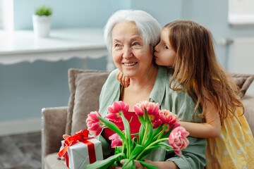 The granddaughter gave her grandmother a bouquet of flowers and a gift on a festive day and kissed her gently