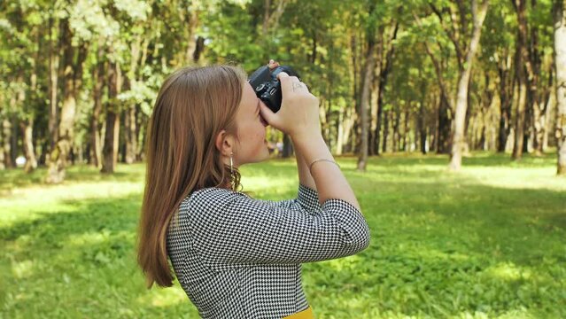 A young girl photographer with a camera poses in the park.