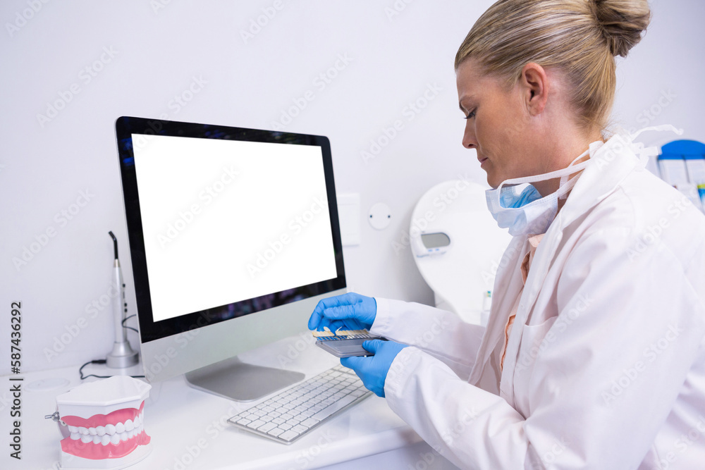 Poster side view of dentist working while sitting by computer