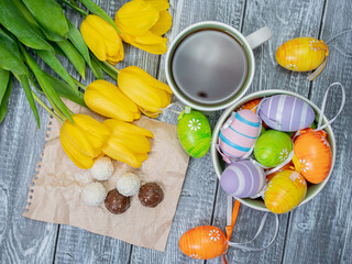 Spring Easter morning with a cup of tea on a wooden table. Yellow tulips and painted Easter eggs