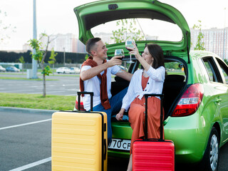 Beautiful young couple with glasses of wine in their hands stand next to the car and suitcases packed for summer travel