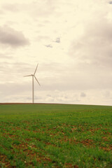 Vertical shot of one white wind turbine in spring time on a cloudy day near a green meadow.