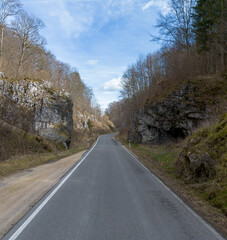 Drone recording of a mountain road in a valley surrounded by rocks and trees in winter.