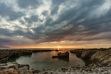 Beautiful sunset on a glass beach by the sea surrounding Sicily and its rocky shores.