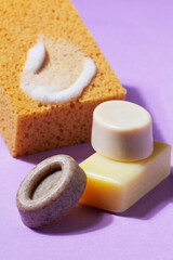 Handmade soap with the addition of coffee and wild herbs and a sponge with foam on a purple background.