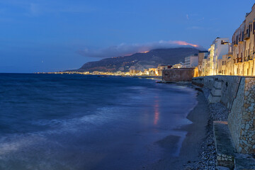 A beautiful seaside small town lit up at night, built right next to a calm sea.