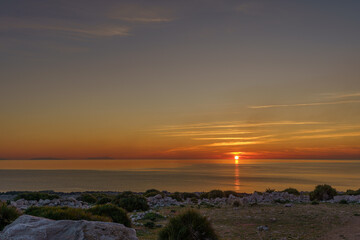 Obraz premium Beautiful sunset on a glass beach by the sea surrounding Sicily and its rocky shores.