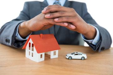 Businessman protecting house model and car with hands on table