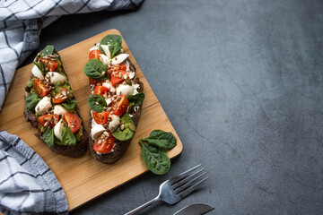 Bruschetta (sandwiches) with cherry tomatoes, mozzarella cheese and herbs on a cutting board on a...