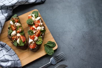 Foto op Plexiglas Bruschetta (sandwiches) with cherry tomatoes, mozzarella cheese and herbs on a cutting board on a dark background. Traditional Italian snack. © Юлия Клюева