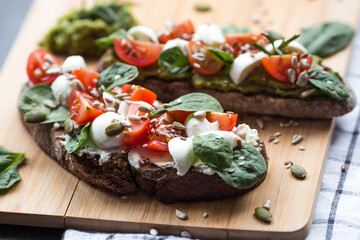 Bruschetta (sandwiches) with cherry tomatoes, mozzarella cheese and herbs on a cutting board on a dark background. Traditional Italian snack.