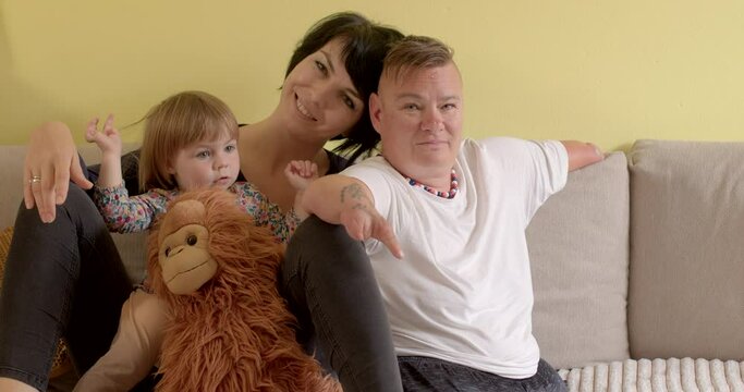 Portrait of parents with cute baby girl at home. Growing up in family. Smiling women posing look at camera, child with monkey toy. Lifestyle indoor. Yellow background