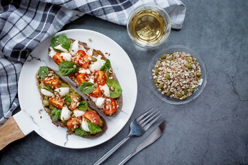 Bruschetta (sandwiches) with cherry tomatoes, mozzarella cheese and herbs on a stylish plate on a dark background. A traditional Italian snack.
