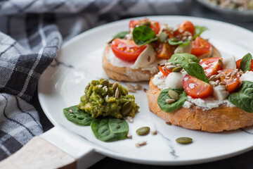 Fototapeta na wymiar Bruschetta (sandwiches) with cherry tomatoes, mozzarella cheese and herbs on a stylish plate on a dark background. A traditional Italian snack.