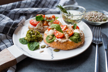 Bruschetta (sandwiches) with cherry tomatoes, mozzarella cheese and herbs on a stylish plate on a dark background. A traditional Italian snack.