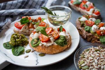 Bruschetta (sandwiches) with cherry tomatoes, mozzarella cheese and herbs on a stylish plate on a dark background. A traditional Italian snack.