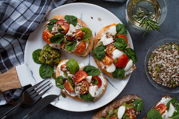 Bruschetta (sandwiches) with cherry tomatoes, mozzarella cheese and herbs on a stylish plate on a dark background. A traditional Italian snack.