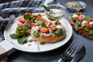 Bruschetta (sandwiches) with cherry tomatoes, mozzarella cheese and herbs on a stylish plate on a dark background. A traditional Italian snack.