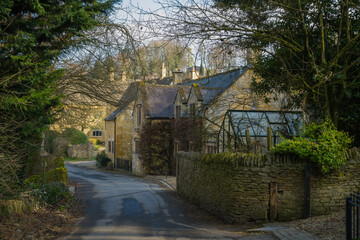 Small road outside old stone built wall and traditional cottage in Cotswolds, England