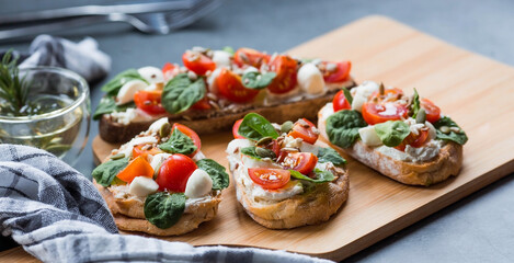 Bruschetta (sandwiches) with cherry tomatoes, mozzarella cheese and herbs on a cutting board on a dark background. Traditional Italian snack.