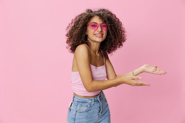 Woman with curly afro hair with sunglasses model poses on a pink background in a pink T-shirt, free movement and dance, look into the camera, smile with teeth and happiness, copy space