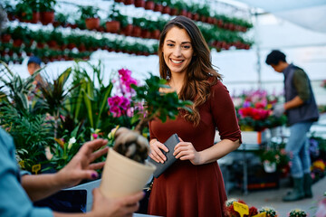 Young happy woman buys pot flowers in greenhouse.
