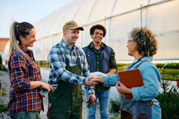 Happy greenhouse worker shaking hands with female quality control inspector.