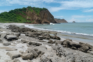 Fototapeta na wymiar a rocky beach of small boulders that are eroded by the constant surf, various other land features such as an mound and cliff in the distance